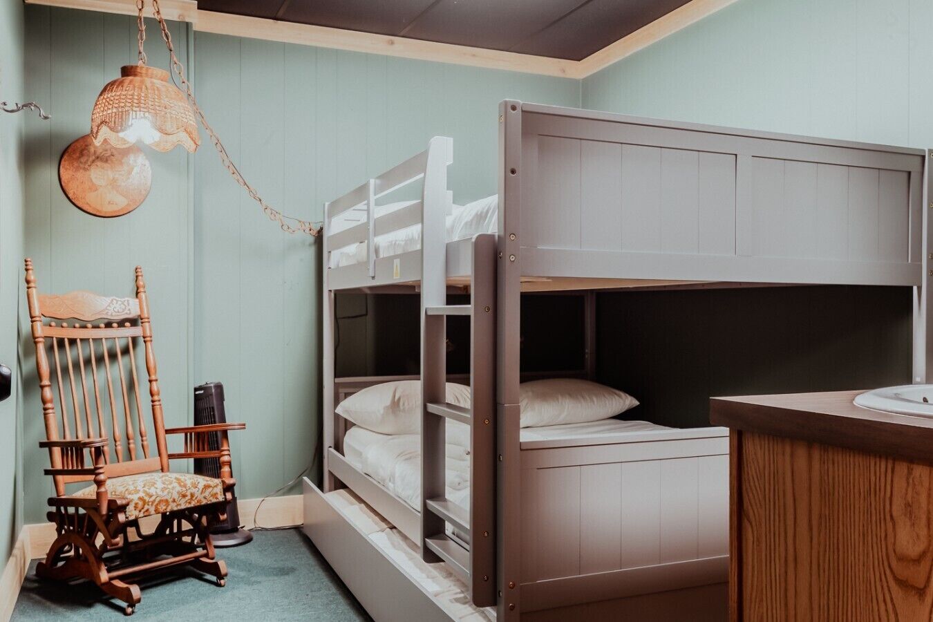 A bunk bed with a wooden headboard, a chair with a cushion, and a hanging light fixture.