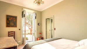 Une chambre à coucher comprenant un lit, une chaise, un bureau, un tableau, une horloge et une porte donnant sur un espace extérieur.