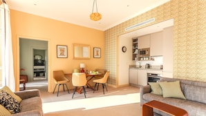 Un salon moderne avec un canapé, une table basse et un coin repas comprenant des chaises et une table. On peut apercevoir la cuisine à travers une porte ouverte.