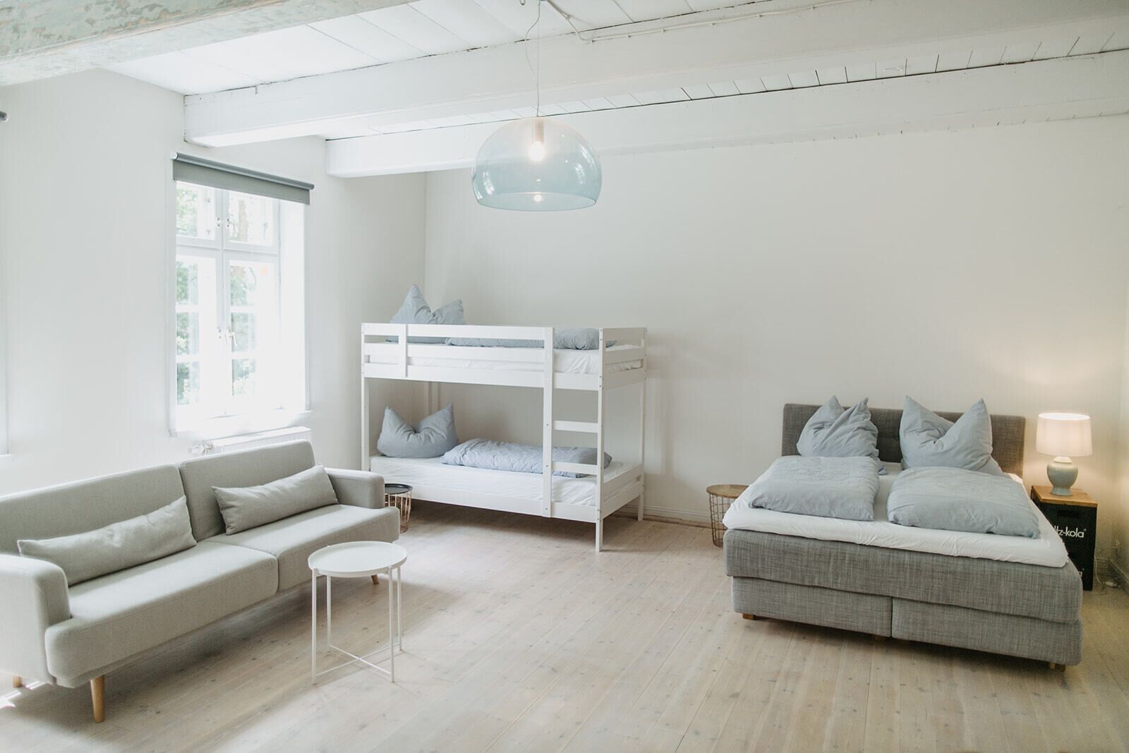 A minimalist bedroom with a bunk bed, a sofa, a small table, and a lamp.