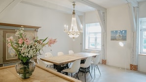 A dining area with a wooden table, white chairs, a chandelier, and a vase with flowers. - North SeaEstate under thatch with sauna near Sankt Peter-Ording / Eiderstedt peninsula (Tetenbüll)