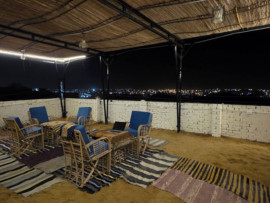Een terras buiten, met een bakstenen muur, blauwe stoelen, een tafel met een laptop en uitzicht op een stadsgezicht 's nachts.