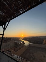 A sunset view from a covered outdoor area with a river and distant hills.