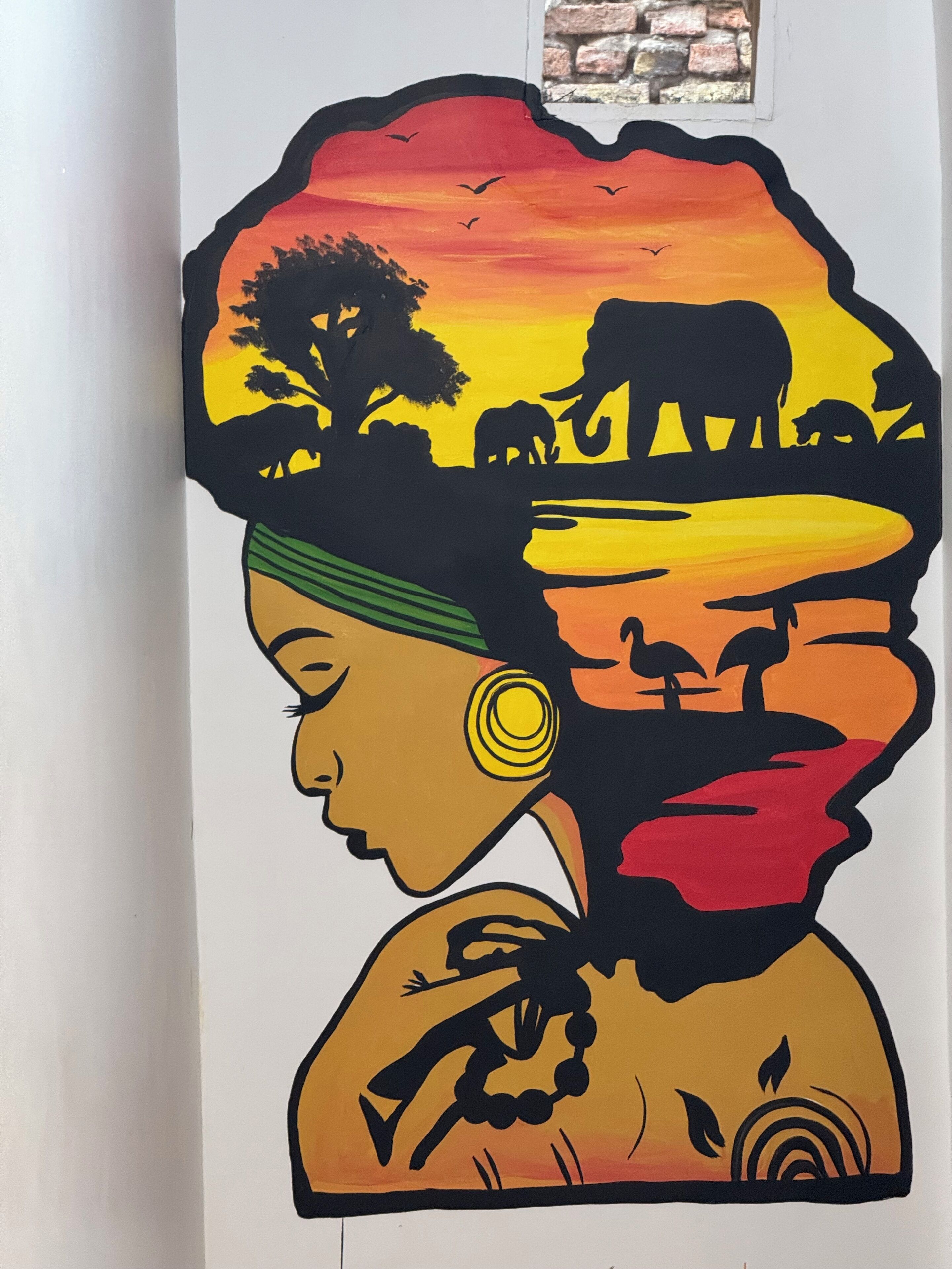 Un muro con un colorido mural que muestra una mujer con pañuelo, animales y una puesta de sol.