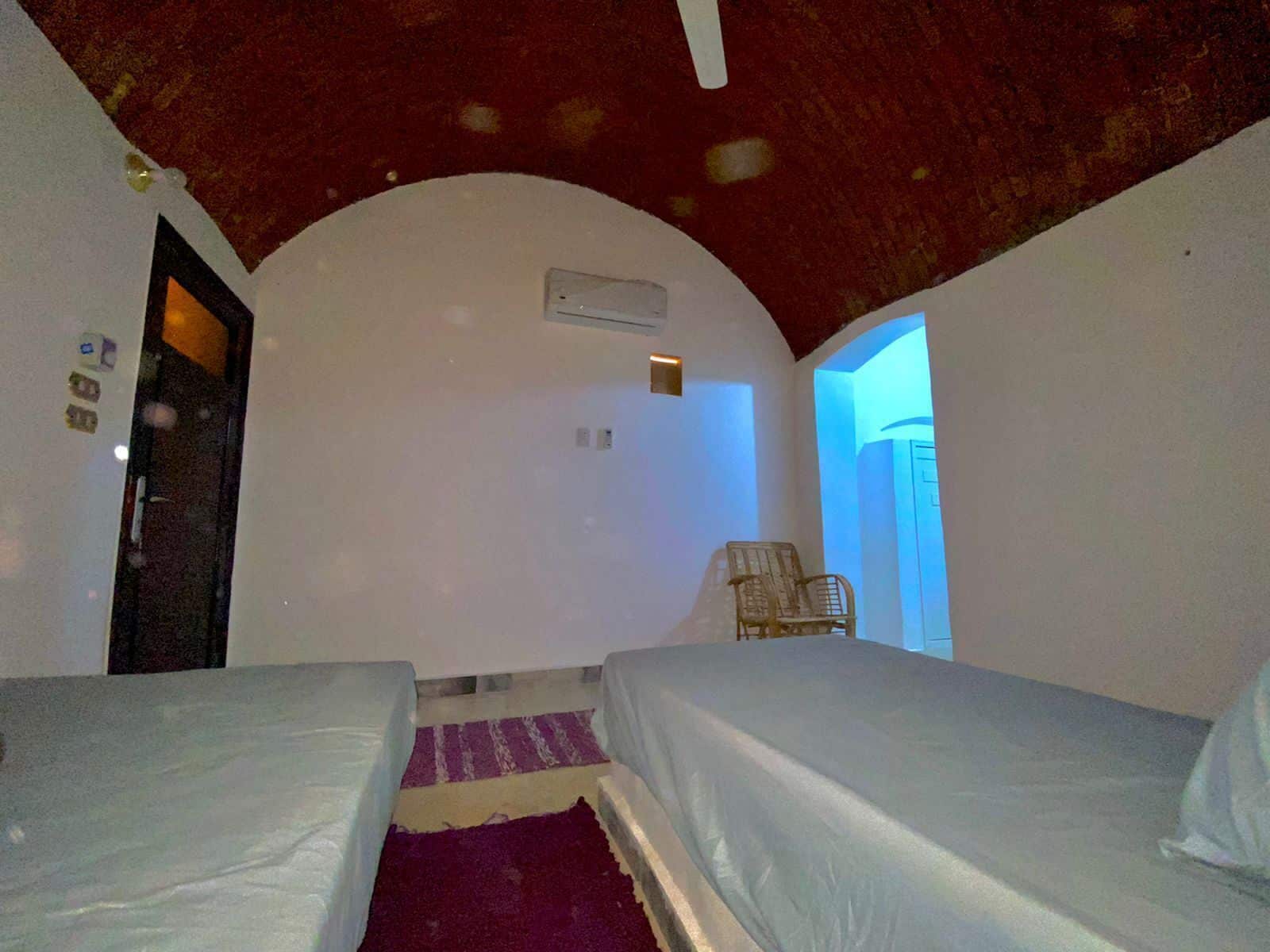 Ein Zimmer mit zwei Betten, einem violetten Teppich, einem Holzstuhl und einer Tür.