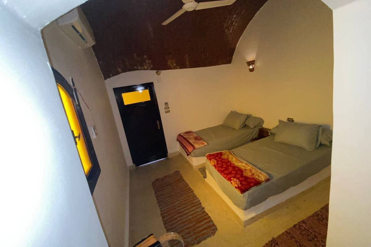 Een slaapkamer met een bed, twee kussens, een plafondventilator, een nachtkastje en een bijzettafeltje.