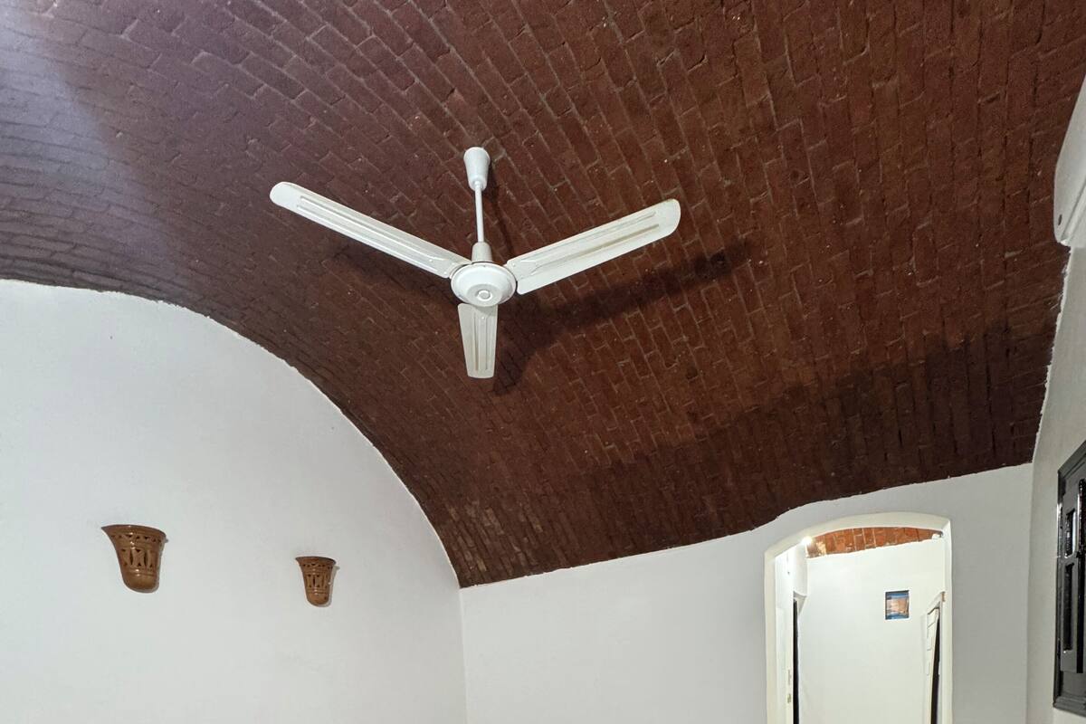Een slaapkamer met een bed, een plafondventilator, een nachtkastje en een gang naar een andere kamer.