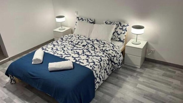 A neatly made bed with a patterned duvet, two bedside tables with lamps, and a wooden floor.