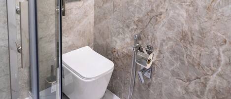 A modern bathroom with a glass shower enclosure, a white toilet, and marble walls.