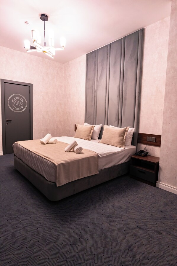 A neatly made bed with a headboard, a bedside table with a phone, and a door with a monogram. - SECRET HOTEL (Baku)