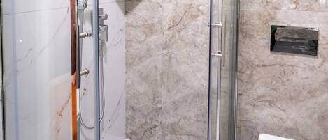 A modern bathroom with a glass-enclosed shower, marble walls, and a toilet.