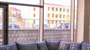 A modern living room with a sectional sofa, a coffee table, and a large window offering a view of buildings and parked cars. - SECRET HOTEL (Baku)