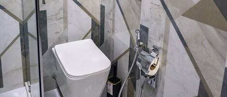A modern bathroom with a glass shower enclosure, a white toilet, and a marble-patterned wall.