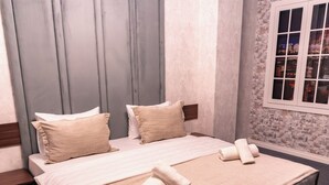 A neatly made bed with beige linens and pillows, a wooden nightstand, and a window with a view of a cityscape at night. - SECRET HOTEL (Baku)