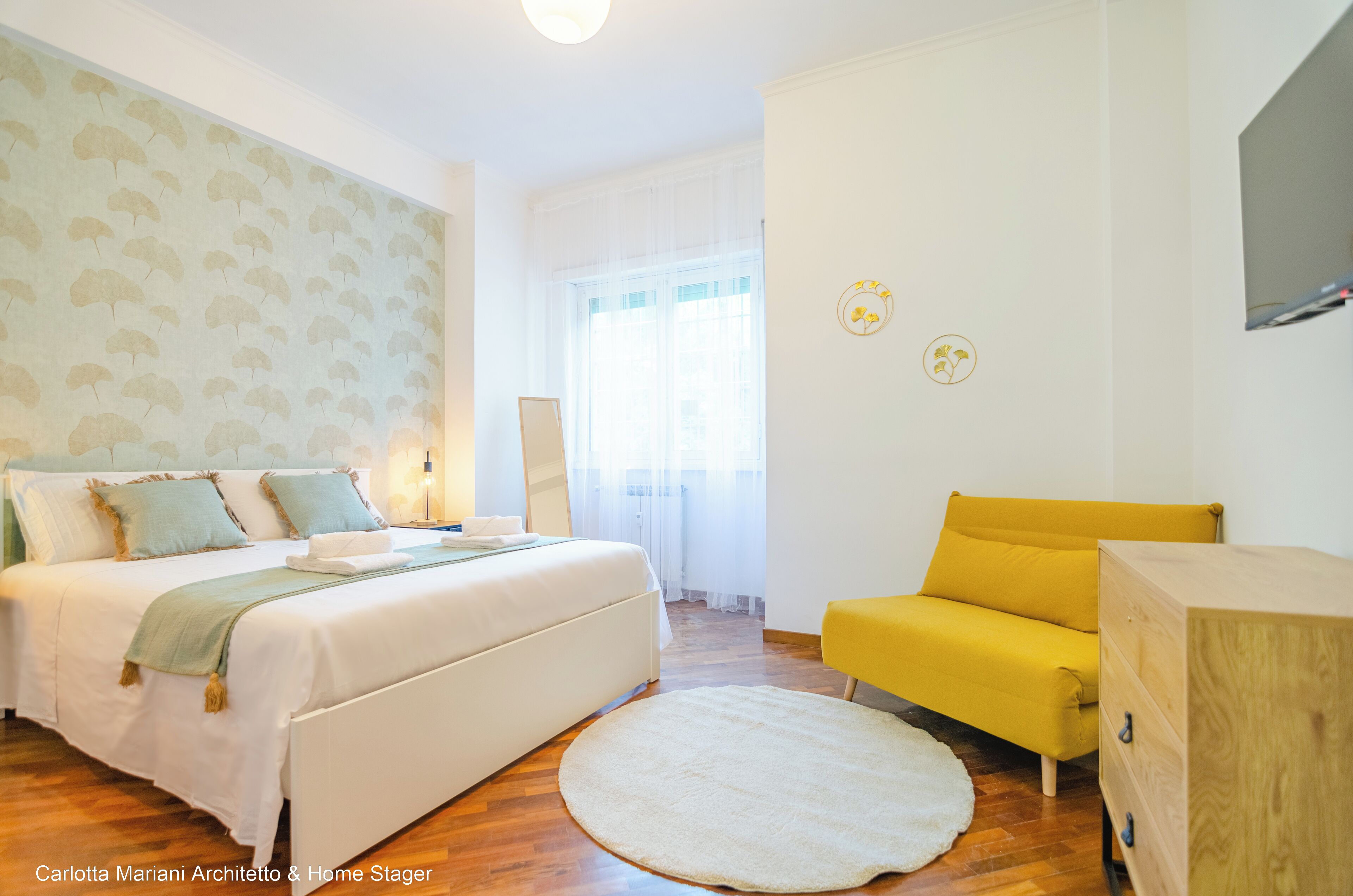 A bedroom with a bed, a yellow chair, a wooden cabinet, and a round rug.