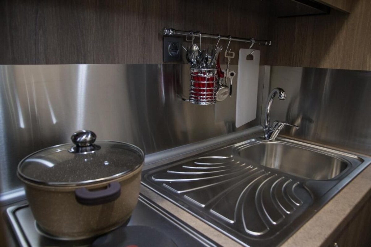 A stainless steel kitchen with a sink, a pot on the stove, and utensils hanging on a rack.