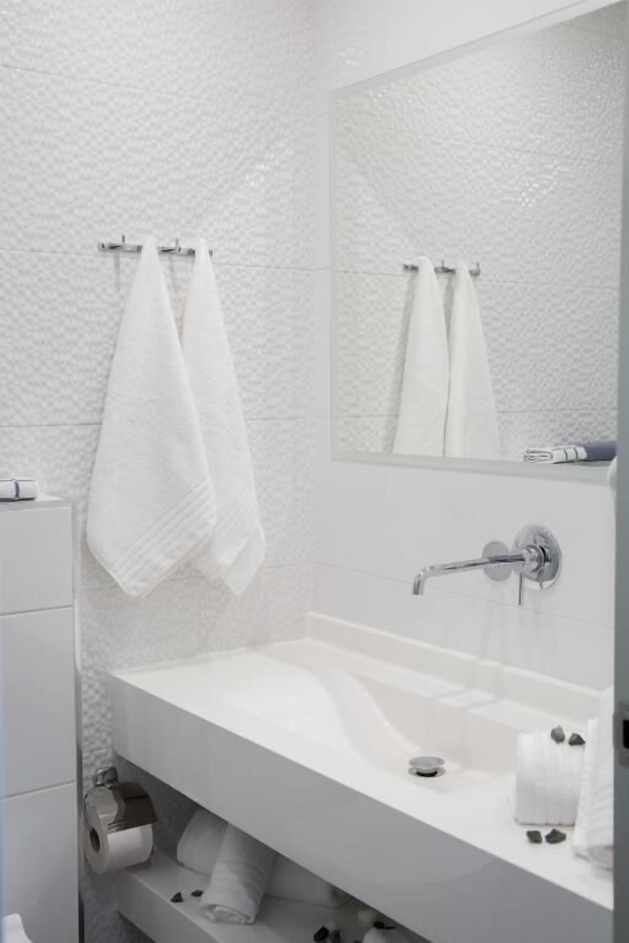 Ein modernes Badezimmer mit einem weißen Waschbecken, einem Spiegel und zwei weißen Handtüchern, die an Haken aufgehängt sind.