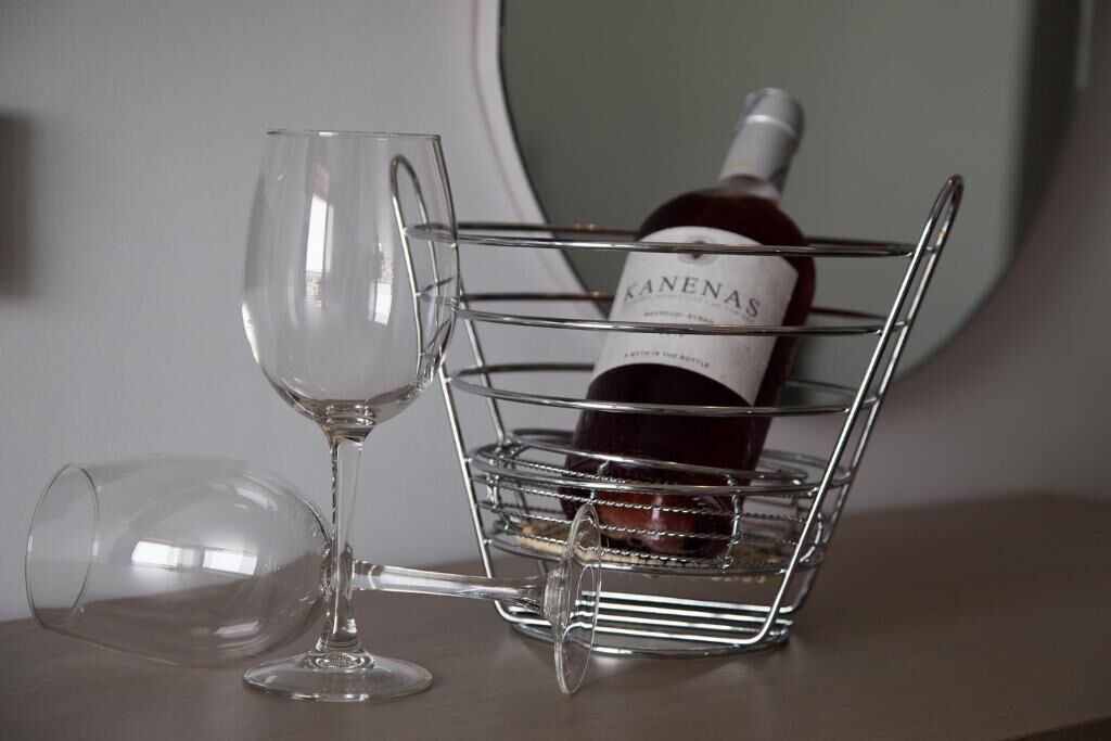 A wine bottle in a wire basket on a table with a wine glass beside it.