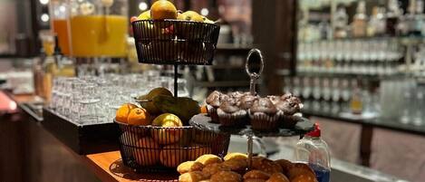 Un bufé de desayuno con diversos pasteles, frutas y un dispensador de jugo.