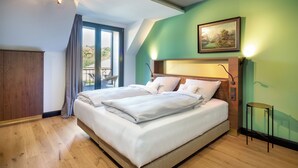 A bedroom with a large bed, a wooden wardrobe, a small table, and a painting on the wall. - HRO Hotel Rittergut Osthoff GmbH (Georgsmarienhuette)