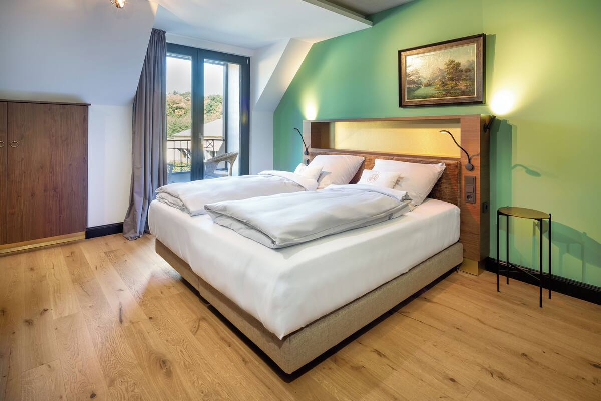 A bedroom with a large bed, a wooden wardrobe, a small table, and a painting on the wall.