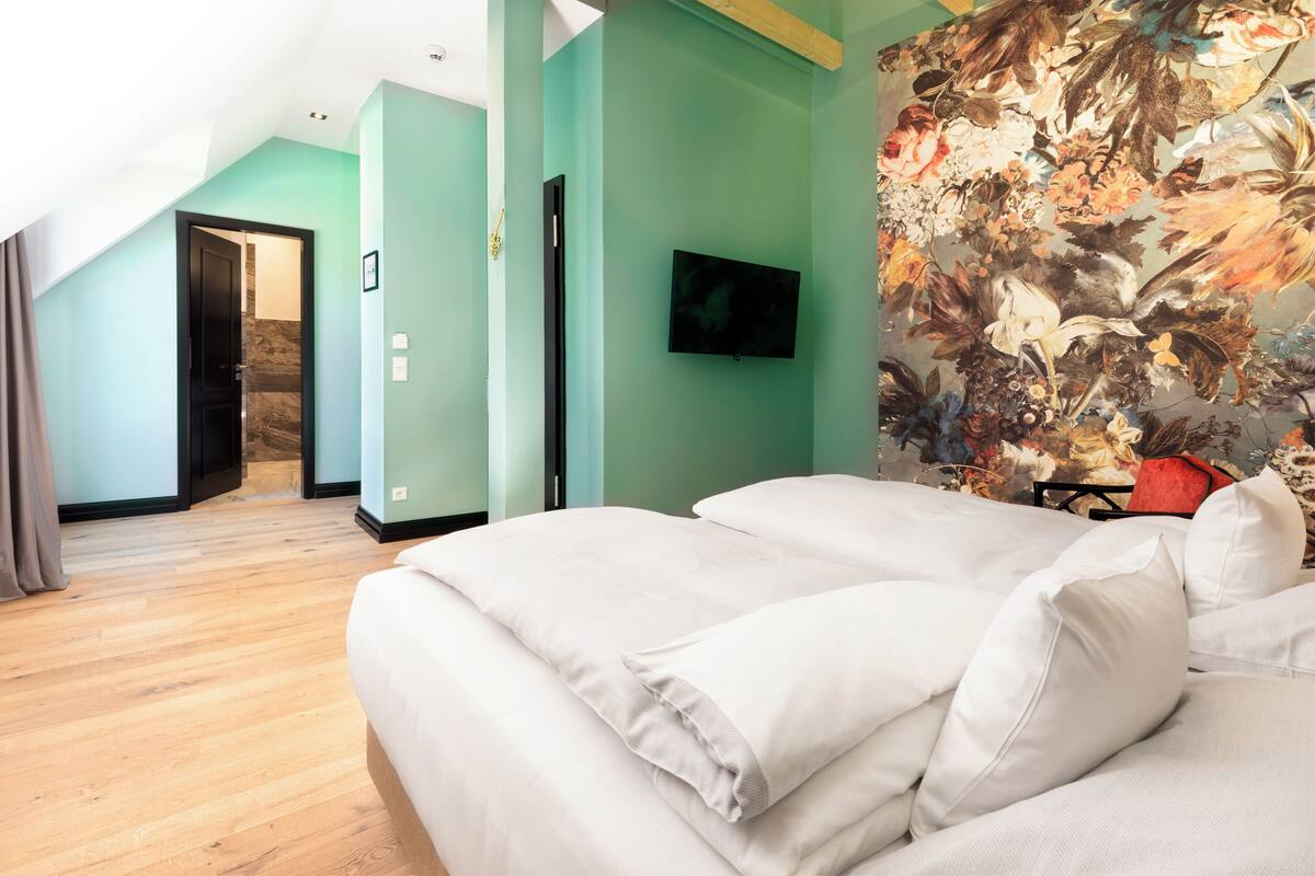 A bedroom with a large bed, a television mounted on the wall, and a floral mural.