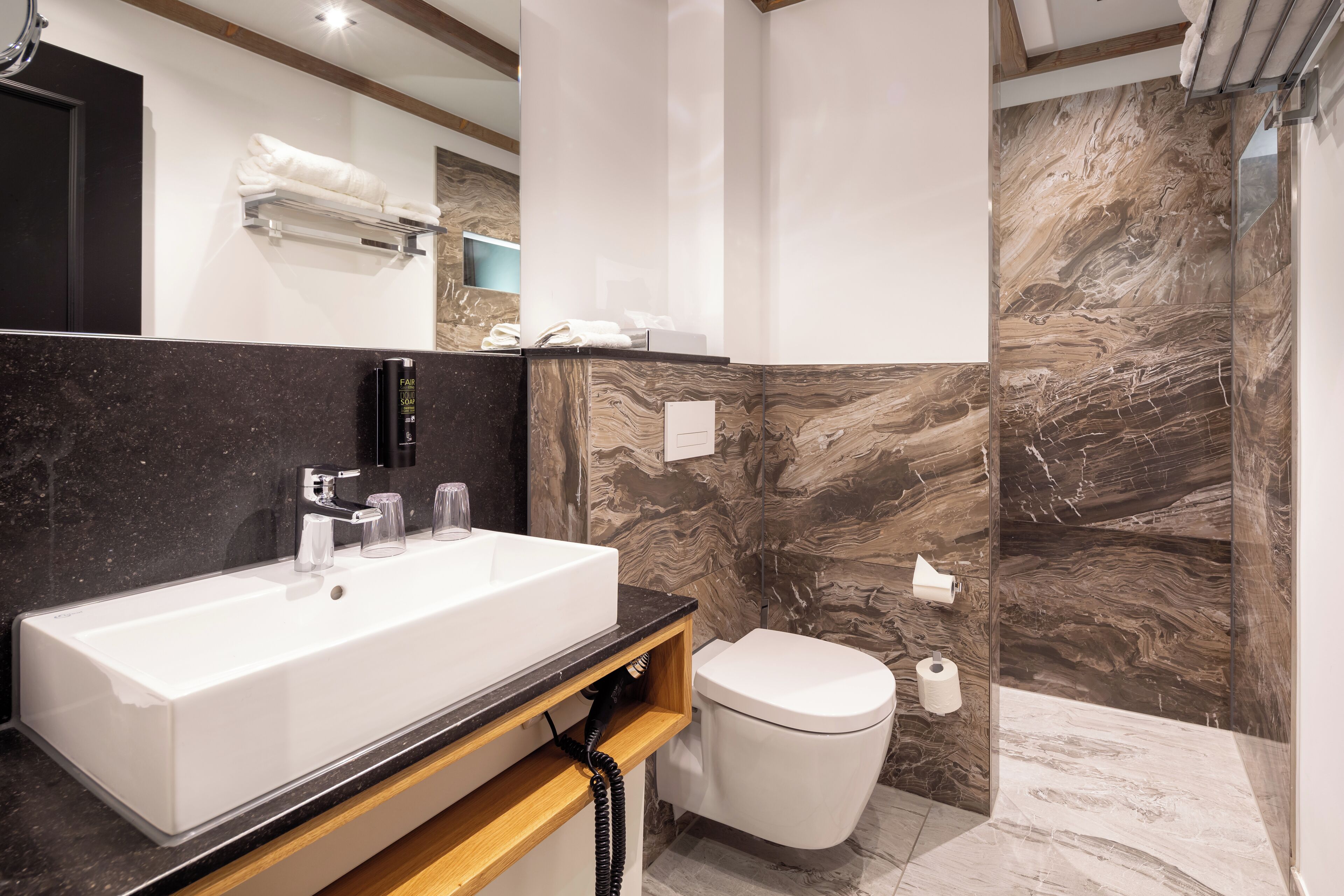 A modern bathroom with a large white sink, a toilet, and marble walls.