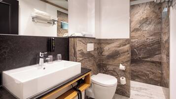 A modern bathroom with a large white sink, a toilet, and marble walls.