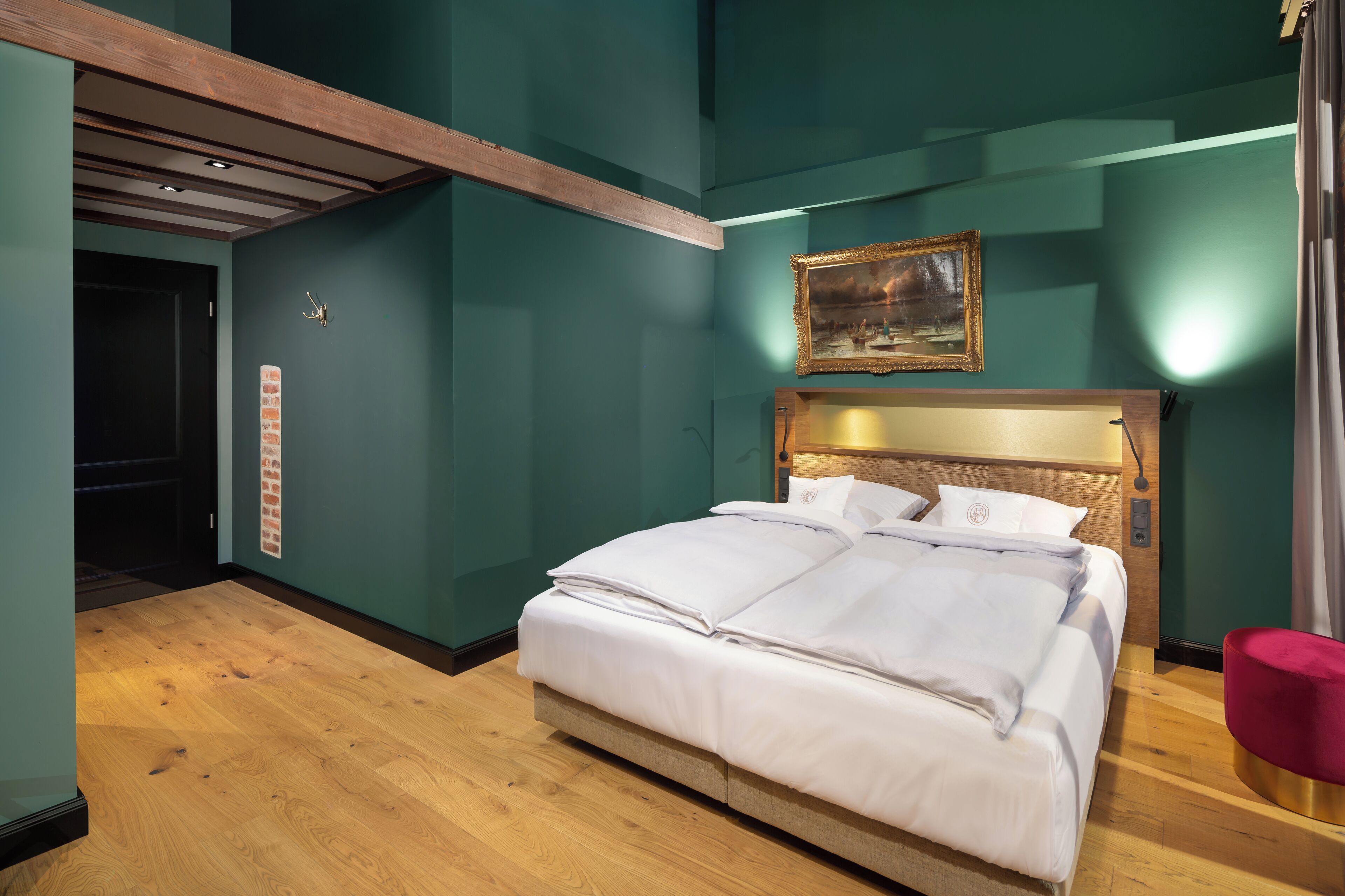 A neatly made bed in a room with teal walls, a wooden floor, and a painting above the bed.