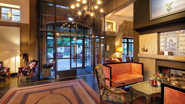 A lobby with a large glass door entrance, a chandelier, and a fireplace with tiled decor. - HRO Hotel Rittergut Osthoff GmbH (Georgsmarienhuette)