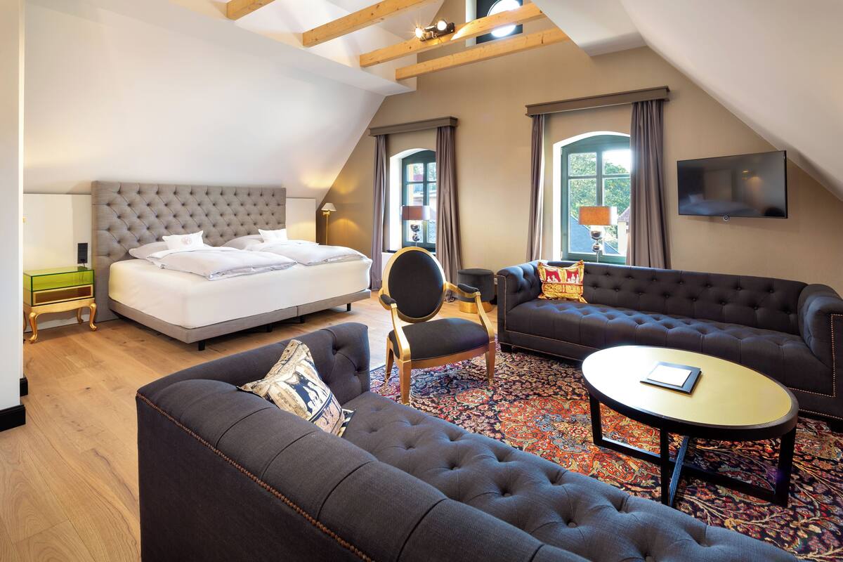 A modern hotel room with a large bed, two sofas, a small table, and a TV.