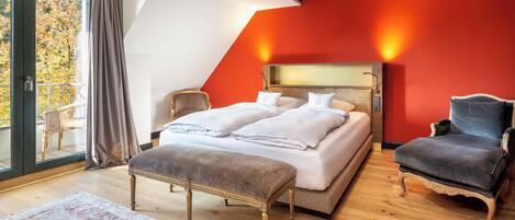 Un dormitorio con una cama, dos sillas, un banco, un ventanal grande y una pared roja.