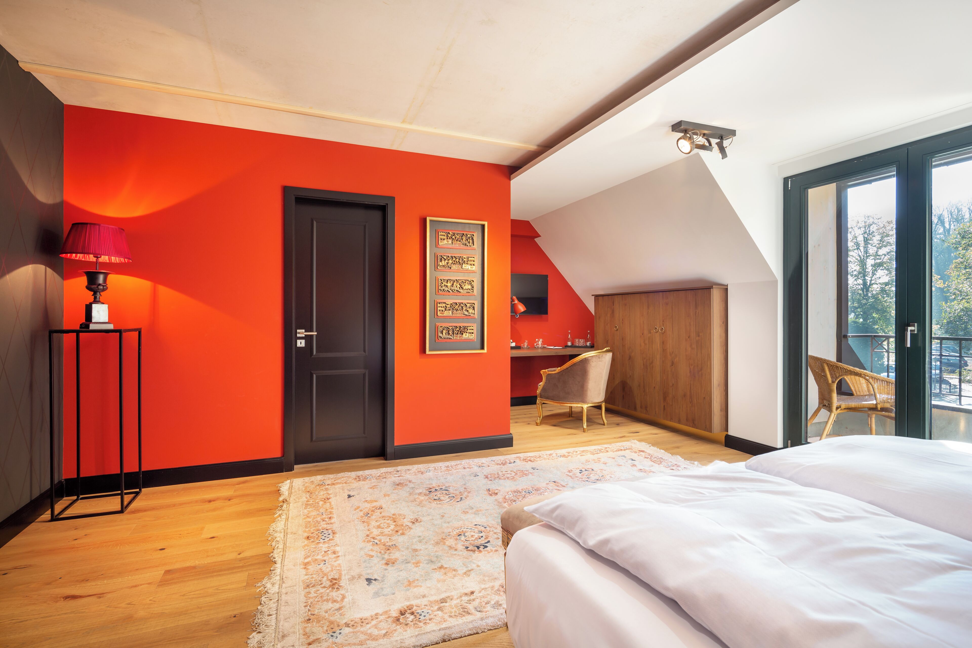Un dormitorio con una pared de acento roja, una cama grande, un escritorio y una silla.