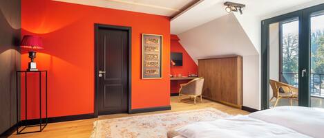 Un dormitorio con una pared de acento roja, una cama grande, un escritorio y una silla.