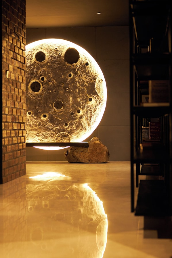 Una gran escultura de luna iluminada en un pasillo con pared de ladrillo y estantería.