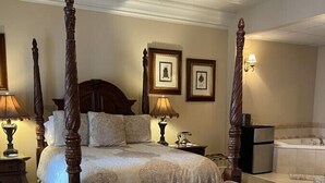 Ein Bett mit Baldachin, ein passendes Sessel, ein großer Spiegel und eine Badewanne in einem gut beleuchteten Zimmer mit gerahmten Bildern an der Wand.