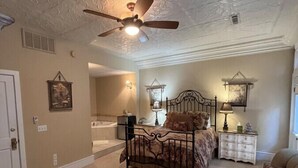 Quarto espaçoso com uma cama grande, ventoinha no teto e vista para um banheiro anexo.