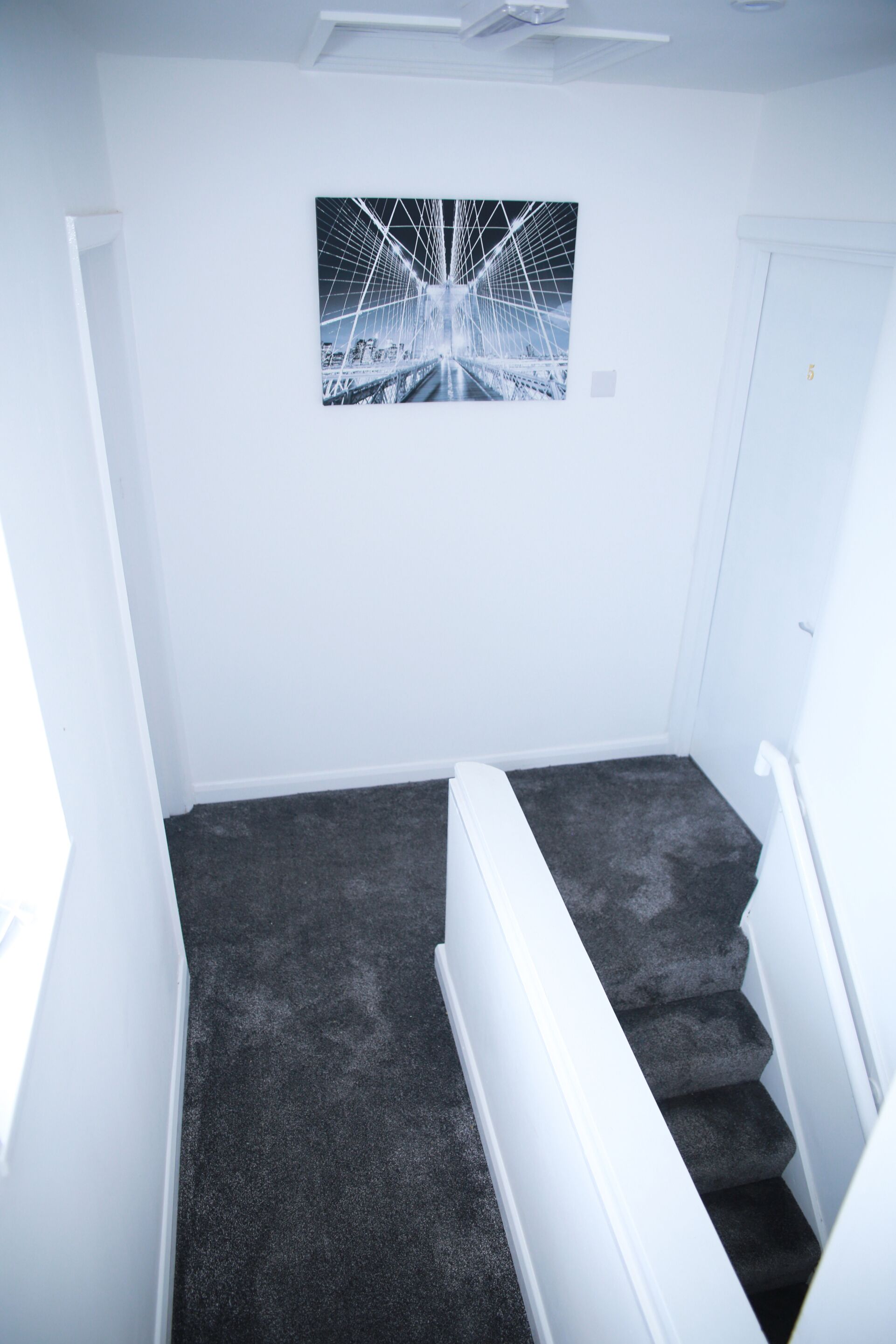 A narrow stairwell with a dark carpet, white walls, and a framed picture of a bridge.