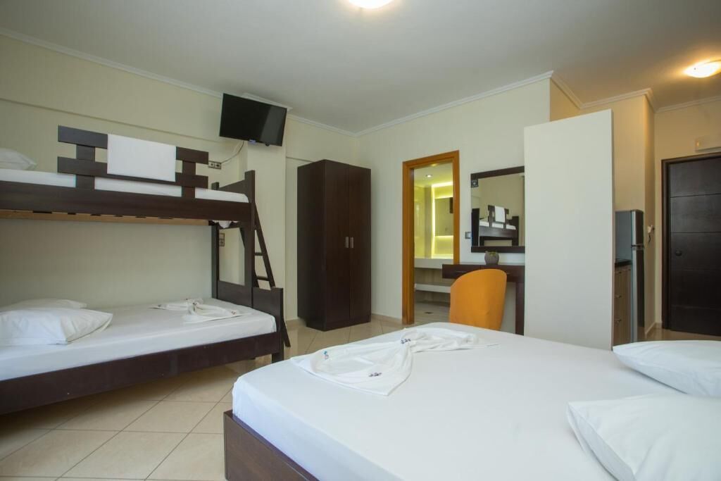 A hotel room with bunk beds, a desk, a chair, a wardrobe, and a television.