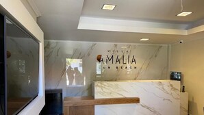 A reception desk with a marble top and a wooden bench. The wall behind the desk has the text "Villa Amalia Sun Beach". - Villa Amalia Sun Beach (Volvi)