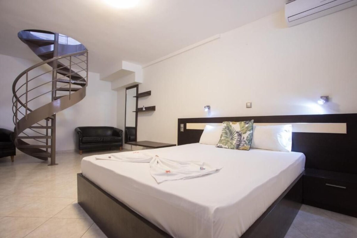 A modern hotel room with a spiral staircase, a large bed with white linens, a black headboard, and a small bedside table.