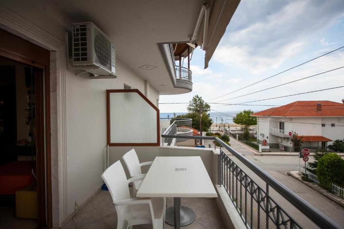 A balcony with a white table and chairs, air conditioning units, and a view of the street and buildings.