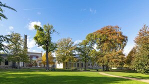 Une cour verdoyante avec un chemin, des arbres et un bâtiment doté d’une haute cheminée.