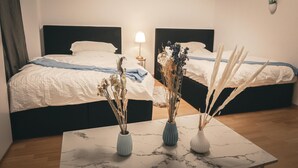 Une chambre d’hôtel avec deux lits, une table de chevet avec une lampe et trois vases contenant des plantes séchées, le tout posé sur une table en marbre.