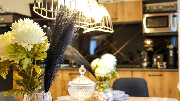 Une table à manger ornée d’un vase de fleurs, d’une lampe décorative, et un four à micro-ondes visible au fond.