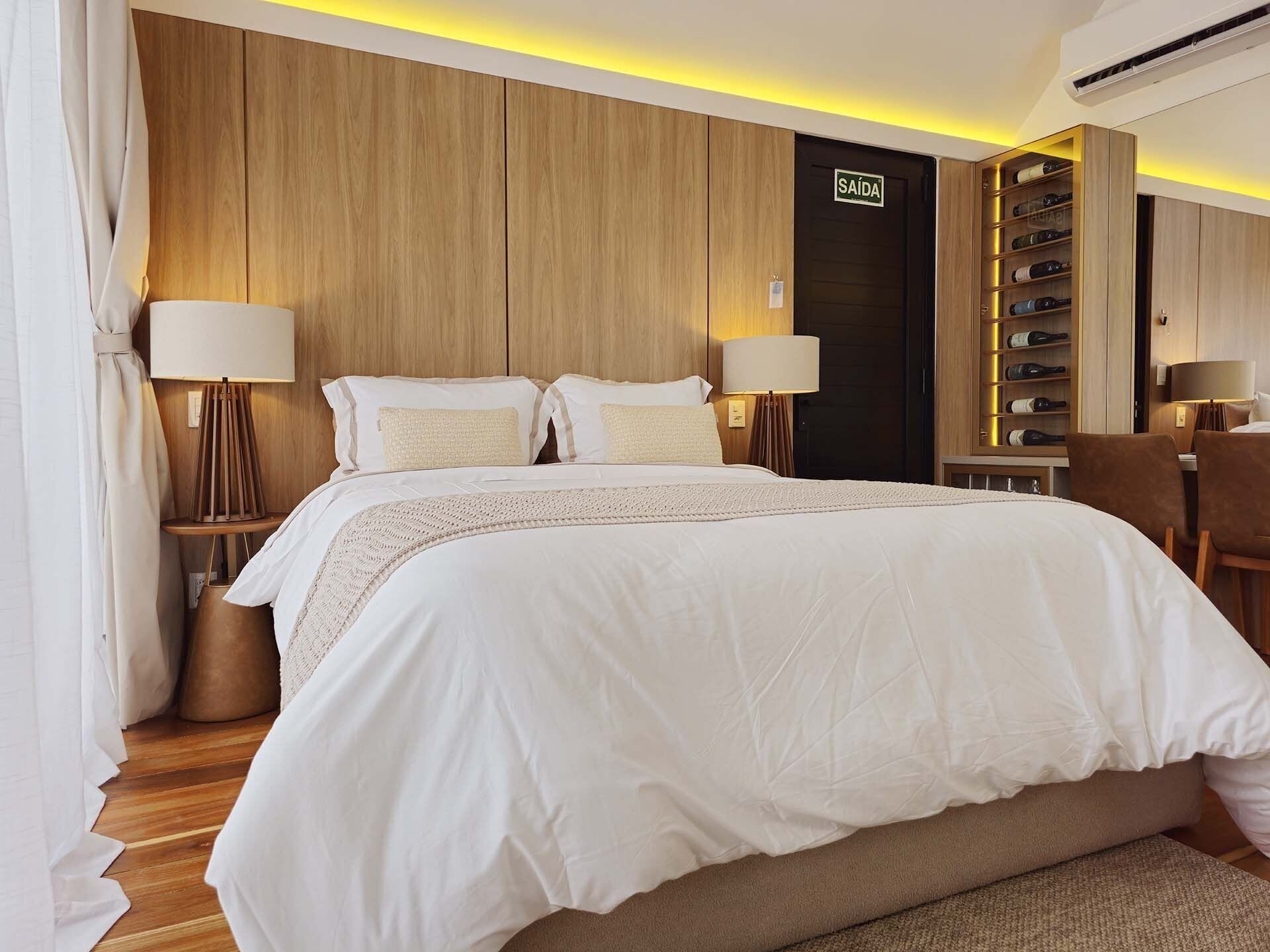 Une chambre d’hôtel avec un grand lit, deux lampes de chevet, un minibar et une porte portant l’inscription « SORTIE ».