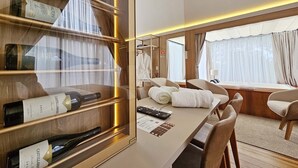 Een moderne hotelkamer met een wijnrek, een eettafel met stoelen en uitzicht op buiten door grote ramen.