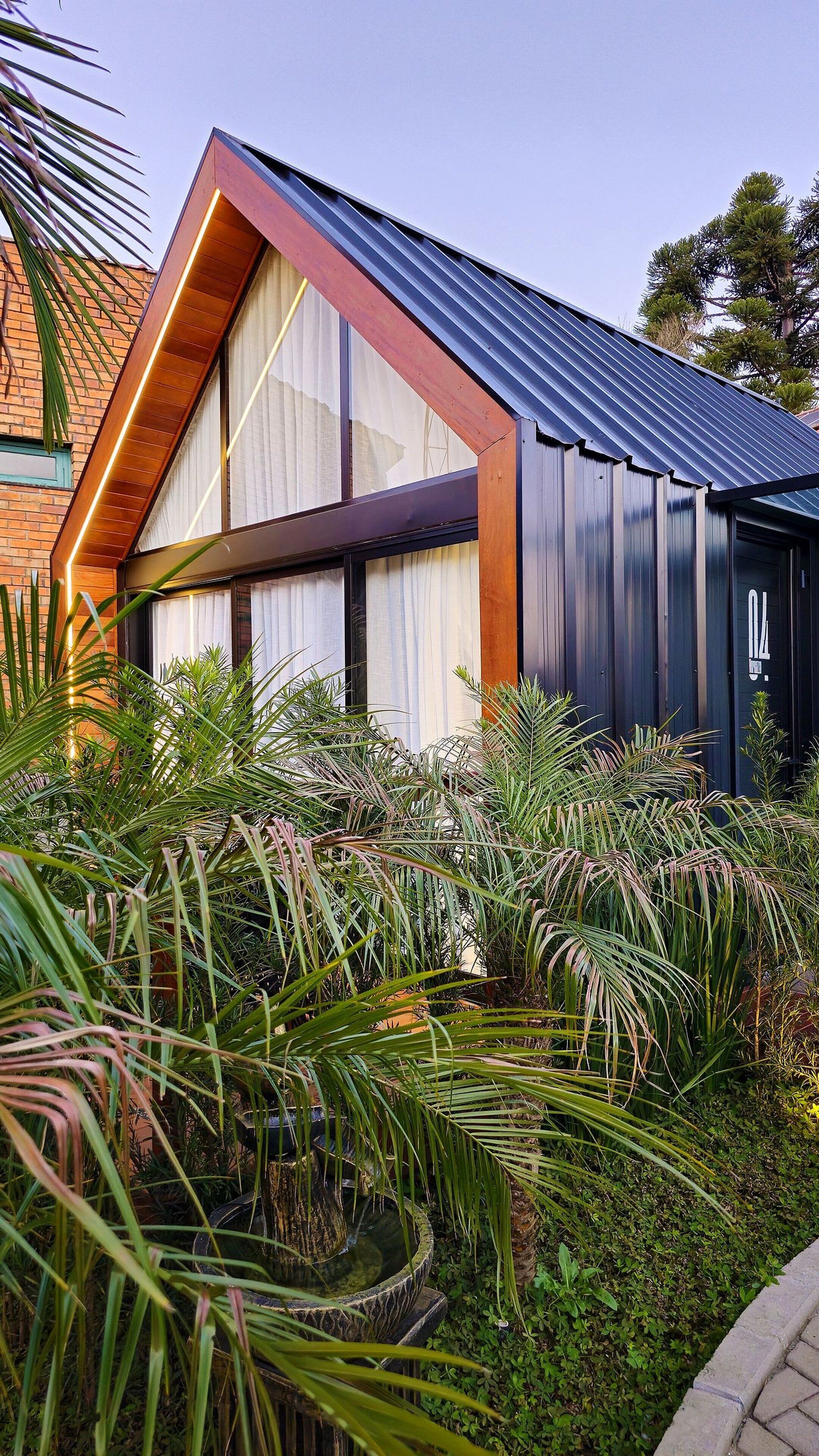 A modern building with large windows, a sloped roof, and a garden with various plants.