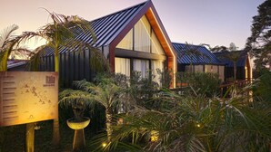 A modern building with a sloped roof, surrounded by lush greenery and a well-lit signboard.