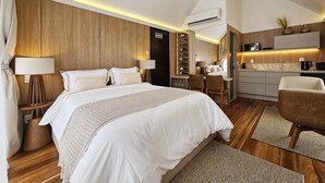 A modern hotel room with a large bed, a built-in wardrobe, a small kitchenette, and a seating area.